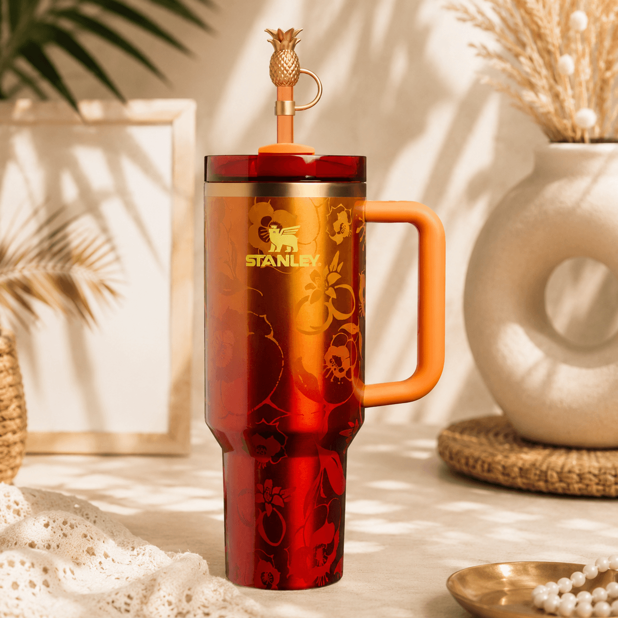 Stanley x Karol G 40 oz Quencher Tumbler in ruby red with floral artwork and pineapple straw topper next to its orange collector box - View 7 | Clistos
